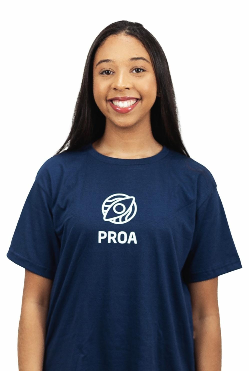 Na imagem, uma jovem mulher está em destaque usando uma camiseta com a palavra PROA em letras grandes. A mulher ocupa a maior parte da imagem, e sua camiseta se destaca em relação aos outros elementos na cena. O texto PROA está localizado na parte inferior central da imagem.